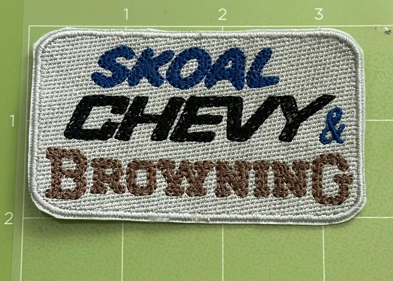 Pu&ograve; includere: Toppa ricamata con le parole "SKOAL CHEVY & BROWNING" in filo blu, nero e marrone su sfondo grigio chiaro. La toppa ha una forma rettangolare con angoli arrotondati e un bordo cucito.