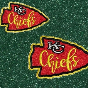 May include: Two embroidered arrowhead-shaped patches featuring a red background with a black and yellow border. Each patch displays the white text KC above the yellow cursive word Chiefs. The design is consistent across both fabric patches.