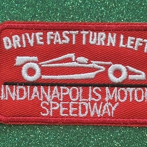 May include: Red rectangular patch with white embroidered text and a race car graphic. The text reads "DRIVE FAST TURN LEFT" above the car and "INDIANAPOLIS MOTOR SPEEDWAY" below.