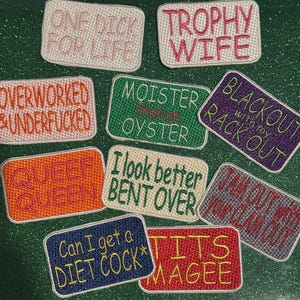 May include: A collection of embroidered patches with various phrases in different colors. The patches include phrases like "ONE DICK FOR LIFE", "TROPHY WIFE", "OVERWORKED & UNDERFUCKED", "MOISTER than an OYSTER", and "BLACKOUT with my RACK OUT".
