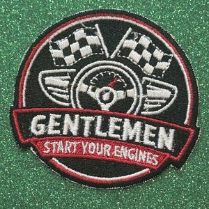 May include: Embroidered patch with a racing theme. The patch is circular, featuring a steering wheel, checkered flags, and the text "GENTLEMEN START YOUR ENGINES" in white and red on a black background.