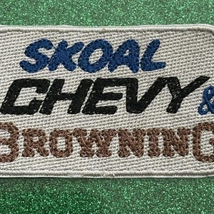 Pu&ograve; includere: Toppa ricamata con le parole "SKOAL CHEVY & BROWNING" in blu, nero e marrone. La toppa ha uno sfondo grigio chiaro e un bordo cucito. La toppa &egrave; rettangolare con angoli arrotondati.