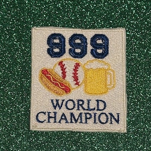 May include: Embroidered patch with the number "999" in navy blue, a baseball, a hot dog, and a mug of beer. The words "WORLD CHAMPION" are embroidered in navy blue below the images. The patch is on a white background.