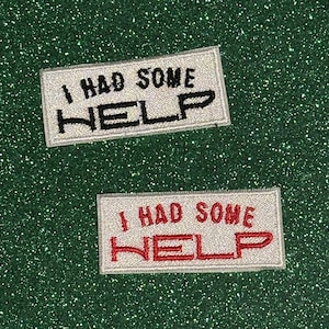 May include: Two rectangular patches with the text "I HAD SOME HELP". One patch has black text, the other has red text. Both patches have a white background and a white border. The background is a sparkly green.