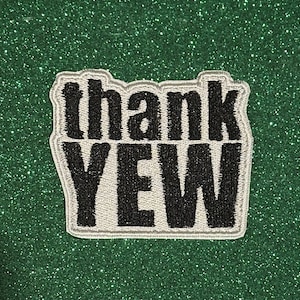 May include: A rectangular patch with the words "thank YEW" in black, outlined in silver, against a green glitter background. The patch is likely an iron-on or sew-on accessory.