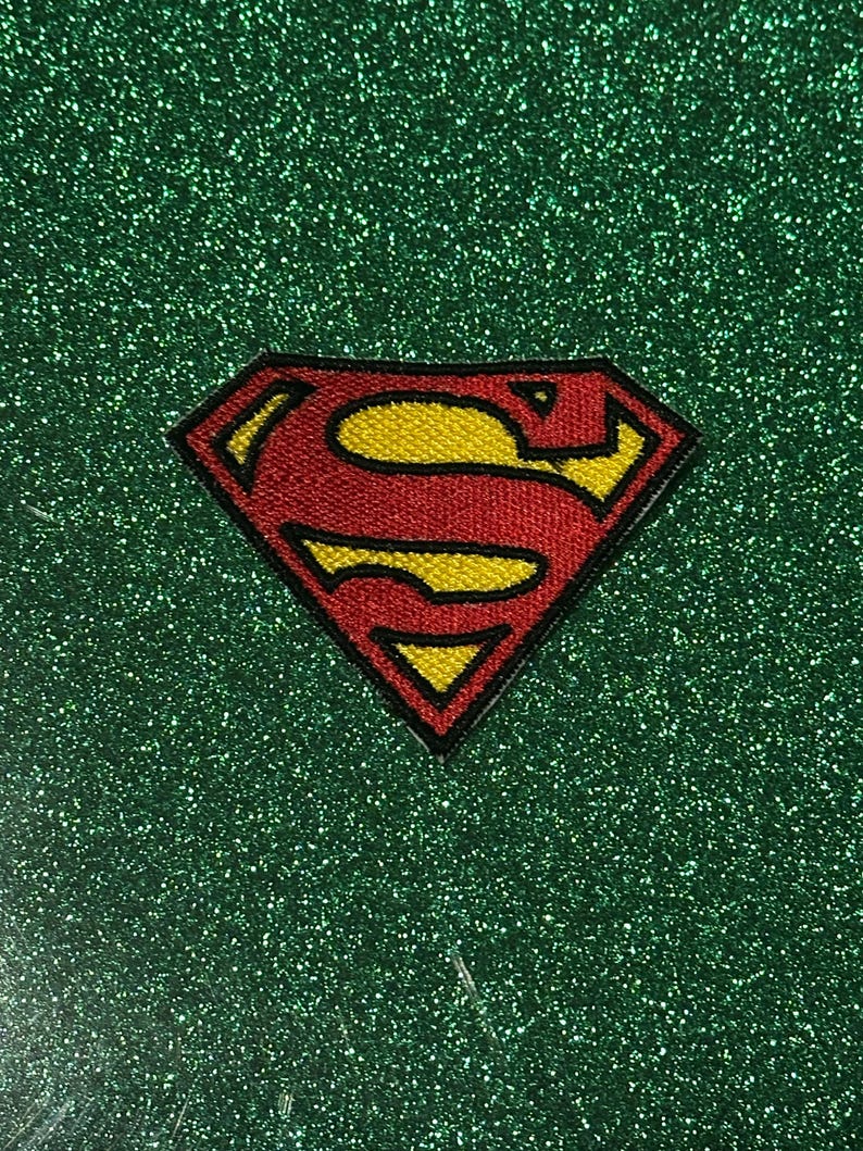 Pu&ograve; includere: Toppa ricamata con il logo di Superman. L'iconico scudo "S" rosso e giallo &egrave; posto su uno sfondo verde glitterato. La toppa presenta un design dettagliato con un contorno nero.