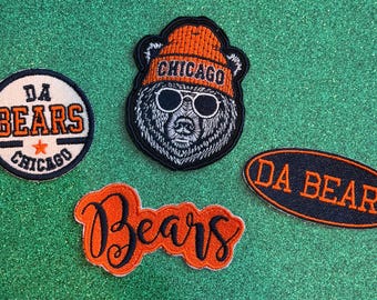 May include: Four embroidered patches featuring Chicago sports themes. One circular patch reads DA BEARS CHICAGO with a star. One bear head patch wears an orange CHICAGO beanie and sunglasses. One oval patch reads DA BEARS. One orange script patch reads Bears.