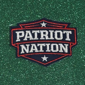 May include: Embroidered patch with the words "PATRIOT NATION" in white, outlined in red, on a navy blue background. The patch has a shield shape with a star at the top and bottom. The background is a sparkly green.