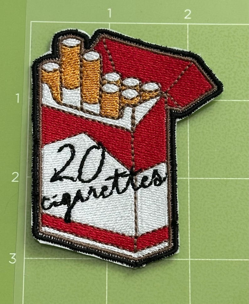 Pu&ograve; includere: Toppa ricamata raffigurante un pacchetto di sigarette. Il pacchetto &egrave; rosso e bianco, con la scritta "20 cigarettes" in nero. Le sigarette sono visibili, con filtri dorati. La toppa ha un bordo nero.