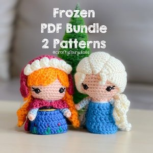 Könnte beinhalten: Zwei gehäkelte Frozen-Puppen, eine mit einem rot-blauen Kleid und orangefarbenem Haar, die andere mit einem blauen Kleid und blonden Haaren. Die Puppen sitzen auf einer weißen Oberfläche mit einem grünen Baum dahinter. Der Text "Frozen PDF Bundle 2 Patterns @craftyfairydolls" befindet sich über den Puppen.