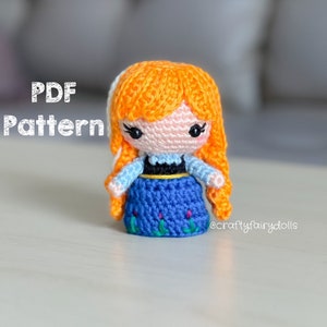 Puede incluir: Patr&oacute;n de crochet para una peque&ntilde;a mu&ntilde;eca con cabello naranja, vestido azul y cintur&oacute;n negro. La mu&ntilde;eca lleva una falda azul con bordados verdes. El patr&oacute;n est&aacute; disponible para descargar en PDF.
