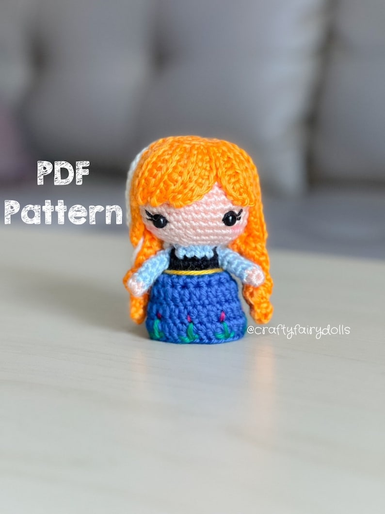 Puede incluir: Patr&oacute;n de crochet para una peque&ntilde;a mu&ntilde;eca con cabello naranja, vestido azul y cintur&oacute;n negro. La mu&ntilde;eca lleva una falda azul con bordados verdes. El patr&oacute;n est&aacute; disponible para descargar en PDF.