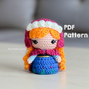 Puede incluir: Patr&oacute;n de crochet para una peque&ntilde;a mu&ntilde;eca con ropa roja, blanca y azul. La mu&ntilde;eca tiene el pelo naranja y una corona blanca. El patr&oacute;n est&aacute; disponible para descargar en PDF. El texto "PDF Pattern" es visible en la imagen.