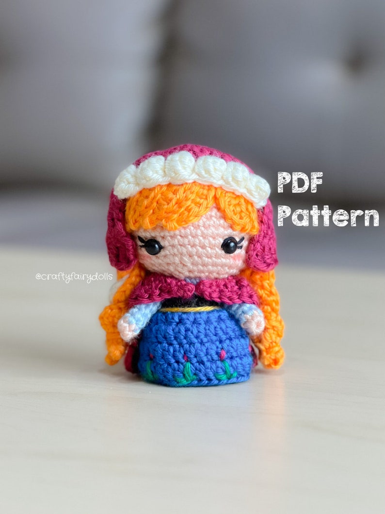 Puede incluir: Patr&oacute;n de crochet para una peque&ntilde;a mu&ntilde;eca con ropa roja, blanca y azul. La mu&ntilde;eca tiene el pelo naranja y una corona blanca. El patr&oacute;n est&aacute; disponible para descargar en PDF. El texto "PDF Pattern" es visible en la imagen.