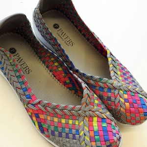 Op de afbeelding: Een paar grijze geweven instapschoenen met een regenboogpatroon. De schoenen hebben een memory foam-inlegzool en de merknaam "PAVERS" staat op de binnenkant gedrukt.