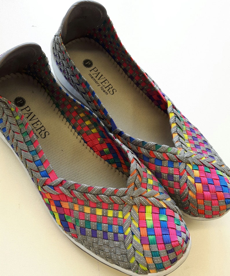 Op de afbeelding: Een paar grijze geweven instapschoenen met een regenboogpatroon. De schoenen hebben een memory foam-inlegzool en de merknaam "PAVERS" staat op de binnenkant gedrukt.