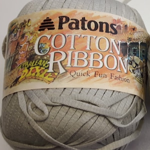 Op de afbeelding: Een bol Patons Cotton Ribbon garen in lichtgrijs. Het etiket luidt "Patons Cotton Ribbon Quick Fun Fashion".