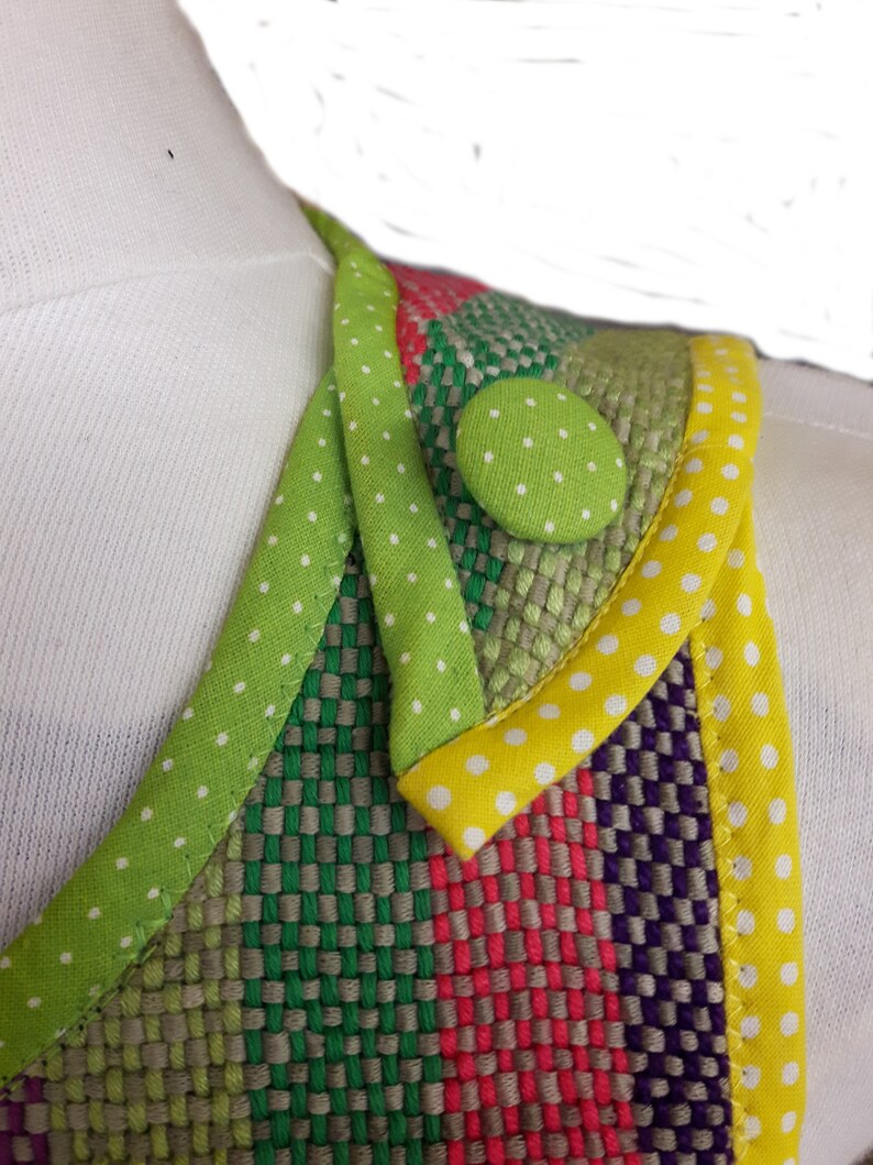 Op de afbeelding: Een close-up van een kleurrijke stof met een groene, gele en witte stippenbies. Een groene knoop met witte stippen is op de stof genaaid.