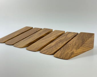 May include: Six wooden door wedges arranged in a row. The wedges are made of a light brown wood with visible grain patterns. Each wedge is approximately 5 inches long and 1 inch high.