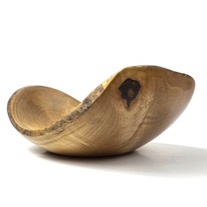 May include: A large, wooden bowl with a natural, light brown finish. The bowl has a unique, asymmetrical shape and a dark brown knot in the wood.