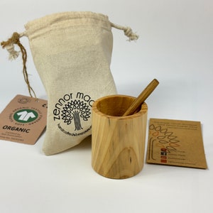 May include: A wooden cup and a wooden stirring stick, both made from natural wood, are displayed on a white surface. The cup is in a small, white drawstring bag. A small card with the text "Handmade with Love" is also visible.
