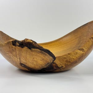 May include: A large, wooden bowl with a natural, rustic finish. The bowl is made from a single piece of wood and has a unique, asymmetrical shape. The wood has a rich, warm color and a beautiful grain pattern.