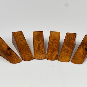 May include: Six wooden doorstops arranged in a fan shape. The doorstops are made of light brown wood with a natural grain pattern.