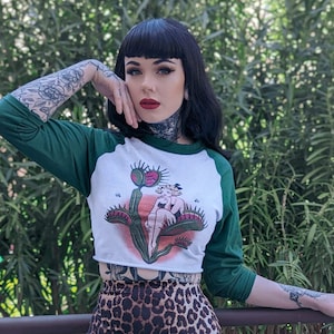 May include: A white and green raglan crop top with a Venus flytrap graphic and a leopard print pencil skirt. The top has green sleeves and a white body. The skirt is a fitted, knee-length style with a brown and black pattern.