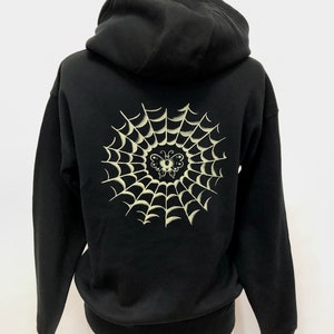 May include: Black hooded sweatshirt with a white spiderweb and butterfly design on the back.