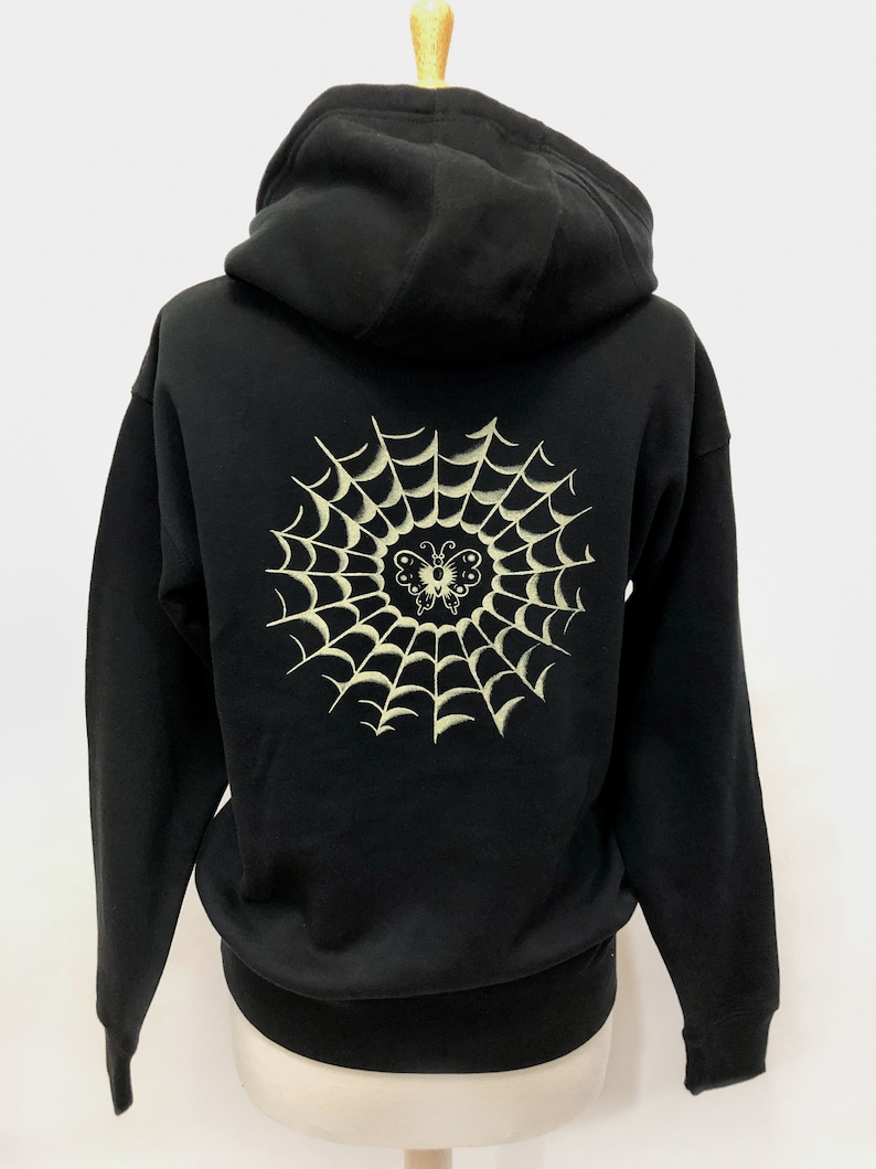 May include: Black hooded sweatshirt with a white spiderweb and butterfly design on the back.