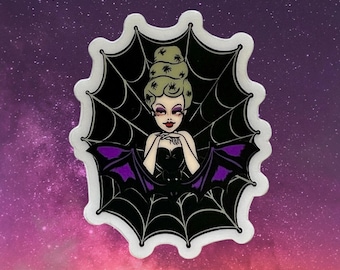 Könnte beinhalten: Ein Aufkleber mit einer Cartoon-Frau mit Fledermausflügeln, umrahmt von einem schwarzen Spinnennetz-Design. Die Frau hat helle Haut, dunkles Haar und trägt ein schwarzes Kleid mit lila Details. Der Hintergrund ist ein Farbverlauf aus Lila und Rosa.