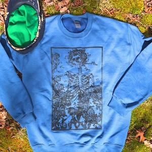 May include: A blue sweatshirt with a black and white graphic print of a skeleton wearing a crown of roses.