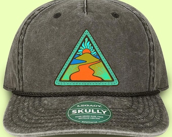 May include: A dark gray baseball cap with a colorful patch featuring a mountain landscape with a sun and winding road. The patch is in a triangle shape with a green border. The hat has a curved brim and a black rope detail.