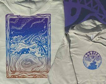 May include: Two off-white hoodies. One features a rectangular design with a bear, butterfly, and celestial elements in blue, purple, and brown. The other has a circular design with an eye, river, and mountains in blue and purple.