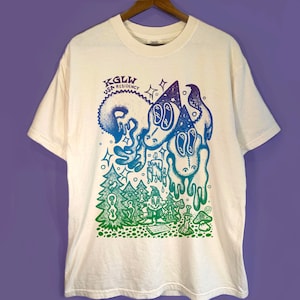 May include: Off-white t-shirt with a colorful graphic print. The design features two cartoonish figures with large eyes, a forest scene, and the text "KGLW USA RESIDENCY". The artwork uses blue, green, and purple hues.