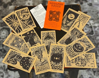 May include: A Hallows Dozen deck of cards featuring tan cardstock with black ink illustrations of occult symbols, a cat, a pumpkin, a cauldron, and a bat. Includes a bright orange instruction card with the text Hallows Dozen.