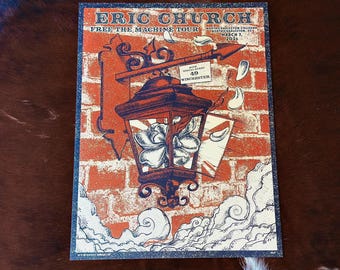 May include: A rectangular concert poster for Eric Church Free The Machine Tour at North Charleston Coliseum on March 7, 2026, featuring a dark blue lantern with a white flower inside, set against an orange brick wall with white clouds below.