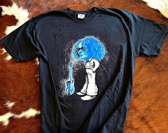 May include: A black short-sleeve t-shirt featuring a graphic print of a person with blue hair and sunglasses standing next to a blue electric guitar. The figure wears a white outfit with the text C369 printed on the chest area of the garment.