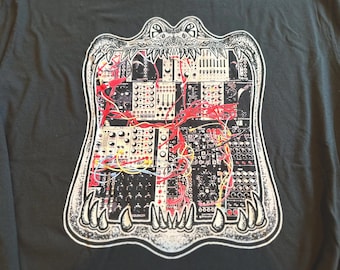 May include: A dark gray t-shirt featuring a white graphic print of an open alligator mouth. Inside the mouth is a detailed illustration of a modular synthesizer system with various black and white control panels and tangled red and yellow patch cables.