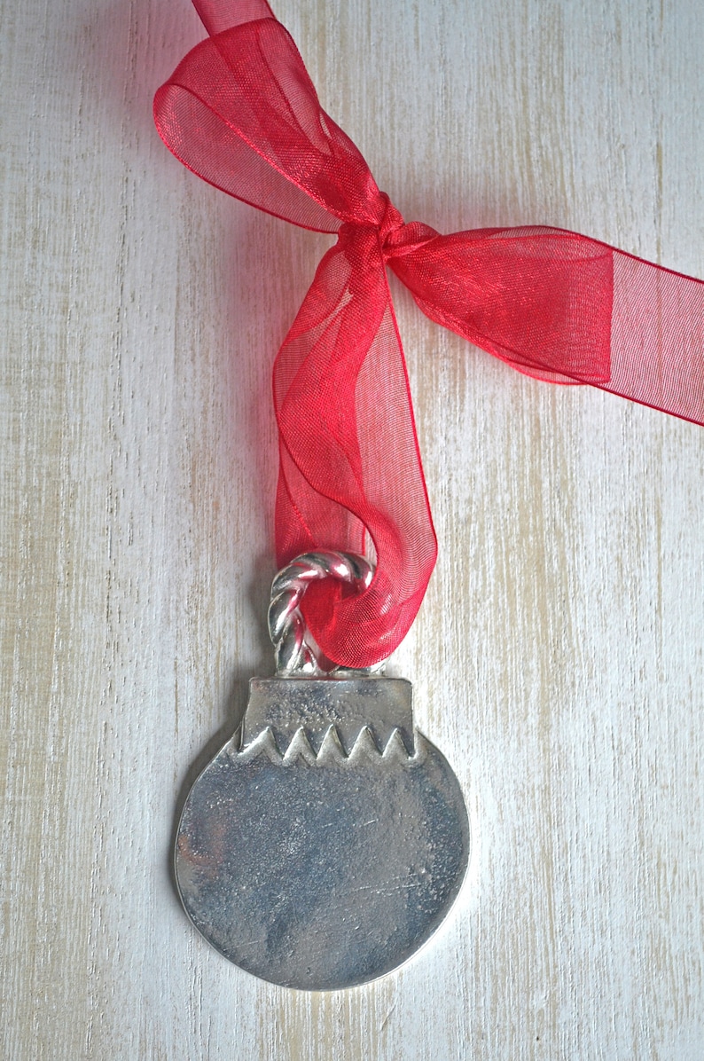 May include: A silver Christmas ornament with a red ribbon tied around the top. The ornament is round and has a textured surface. The ribbon is made of sheer fabric and has a bow tied at the top.