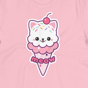 K&ouml;nnte beinhalten: Hellrosa T-Shirt mit einem Cartoon-Eiswaffel-Katzen-Design. Das Eis hat Streusel, eine Kirsche und das Wort "meow". Das T-Shirt ist aus einem weichen Material. Ein lustiges, l&auml;ssiges Oberteil.