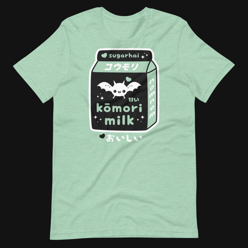 May include: A light green t-shirt featuring a graphic of a black milk carton with a bat illustration and Japanese text. The text includes "sugarhai", "kōmori milk", and "delicious". The design has a cute, kawaii aesthetic.
