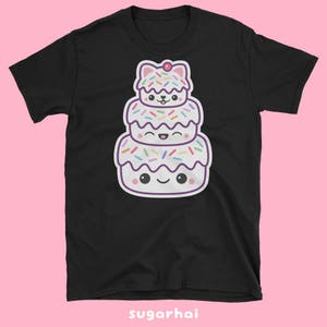May include: Black t-shirt featuring a stacked cartoon dessert with a cat-like shape on top. The dessert has white frosting, colorful sprinkles, and smiling faces. The text "sugarhai" is at the bottom.