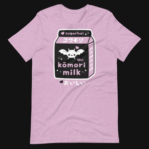 May include: A light pink t-shirt featuring a black and white graphic of a milk carton with a bat and the words "kōmori milk" in Japanese characters. The shirt also has the text "sugarhai" and "美味しい".
