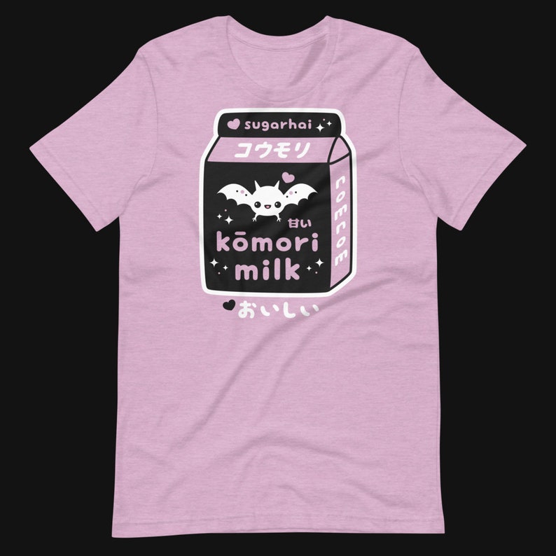 May include: A light pink t-shirt featuring a black and white graphic of a milk carton with a bat and the words "kōmori milk" in Japanese characters. The shirt also has the text "sugarhai" and "美味しい".