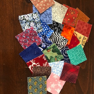 May include: A collection of 20 fabric squares in various colors and patterns, including floral, polka dot, paisley, and geometric designs. The squares are arranged in a random pattern on a wooden surface.