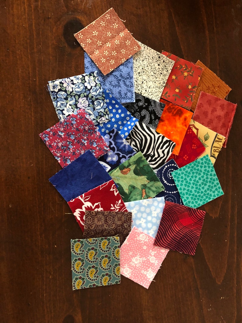 May include: A collection of 20 fabric squares in various colors and patterns, including floral, polka dot, paisley, and geometric designs. The squares are arranged in a random pattern on a wooden surface.