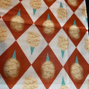 May include: Cotton candy print fabric featuring a repeating pattern of cotton candy cones on a diamond grid. The cotton candy is light yellow, the cones are blue and white, and the diamonds are red and white.
