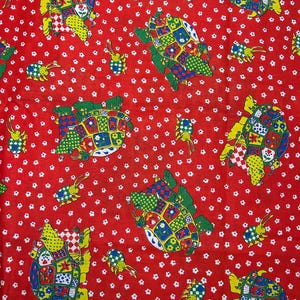 May include: A vibrant red fabric featuring a repeating pattern of colorful turtles and small, bug-like creatures. The turtles have patchwork-style shells with various patterns and colors, including yellow, green, blue, and red. The background is dotted with small white floral shapes.