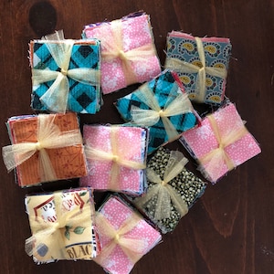 May include: A collection of fabric squares, each tied with a yellow ribbon, are stacked on a wooden surface. The fabric squares are in various patterns and colors, including pink, blue, green, and brown.